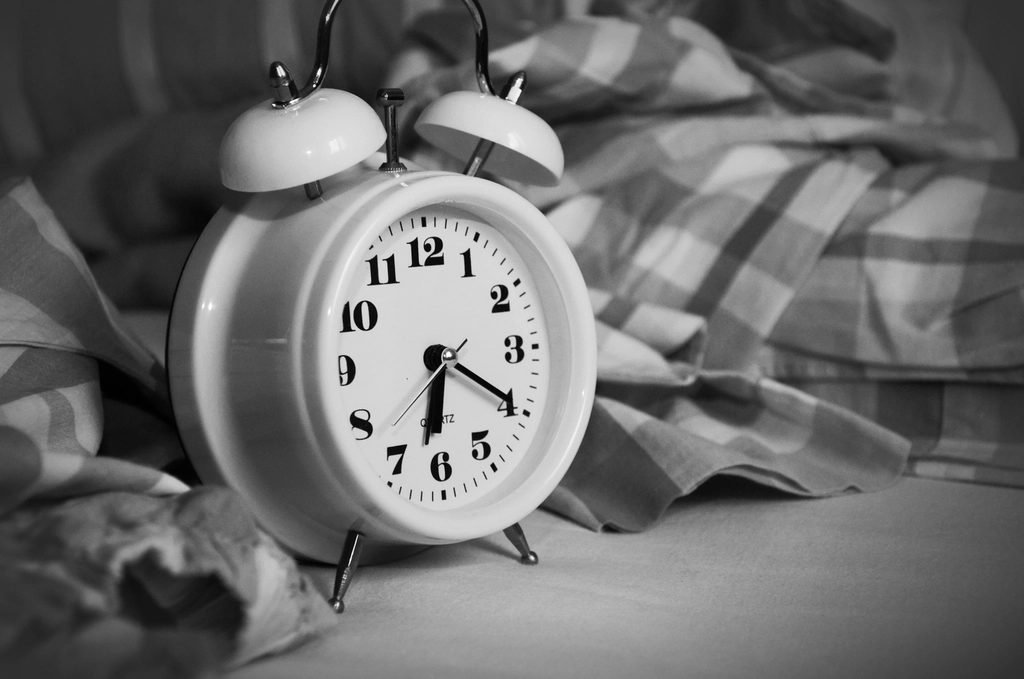 Alarm clock on a nightstand beside a bed, representing timing a wake-up around sleep cycles